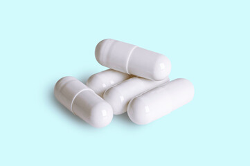 Group of white capsule pills on light blue background.