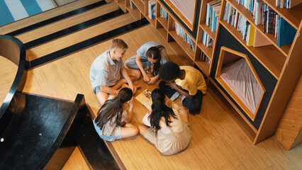 Top view of diverse children sitting in circle while looking at camera and waving hands at library...