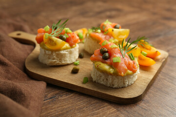 Tasty canapes with salmon served on wooden table, closeup