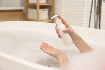 Woman applying shower gel onto hand in bath indoors, closeup. Space for text