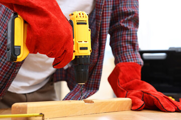 Young handyman working with electric drill at table in workshop, closeup