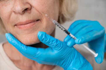 Doctor makes beauty injections in the face of an old caucasian woman. Cropped portrait. 
