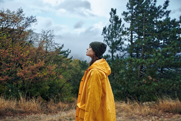 A woman in a yellow raincoat enjoying a peaceful moment surrounded by nature and trees in the field...