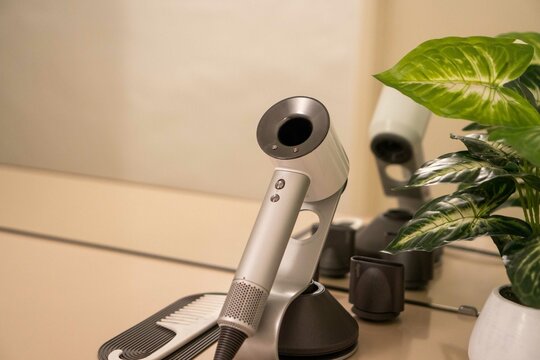 Modern Dyson hair dryer and comb on vanity beside green houseplant.