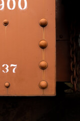 Rustic and Rusty heavy steel wall, fastened with large rivets. Orange and green paint on the side of a vintage train car. Corrosion eats away at the metal