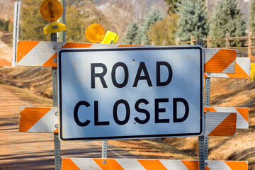 There is orange striped road closure sign near an ongoing construction project that preventing vehicles from driving
