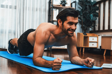 Athletic and sporty man doing plank on fitness mat during home body workout exercise session for...