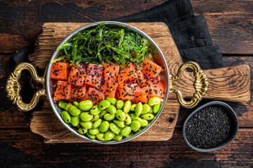 Salmon poke bowl with fresh fish, rice, seaweed, edamame, black sesame. Wooden background. Top view