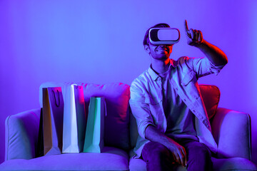 Caucasian man with vr glass posing pointing finger while sitting at sofa with shopping bags. Person...