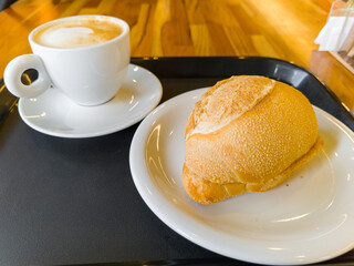Cappuccino and Fresh Bread Roll on a Café Table.