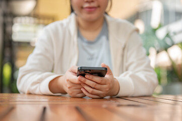 A cropped image of a young positive Asian woman using her smartphone at an outdoor table of a cafe.