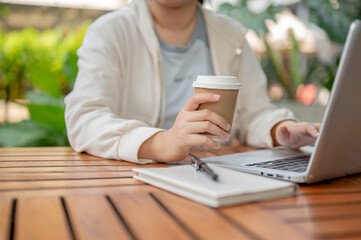 An Asian woman working remotely at a cafe, sipping coffee while working on her computer.