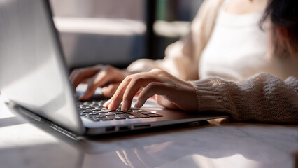 Close-up image of a woman typing on keyboard, working on her laptop computer at a table indoors.