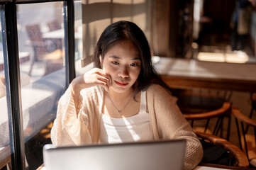 Young thoughtful Asian woman working remotely at a coffee shop, pensive planning about her job.