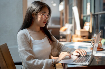 A woman is focusing on her work on her laptop computer, sitting at an outdoor table of a cafe.