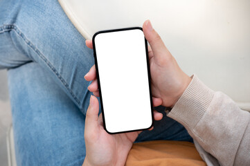 A close-up image of a woman in jeans sits outdoors on a sunny day and uses her smartphone.