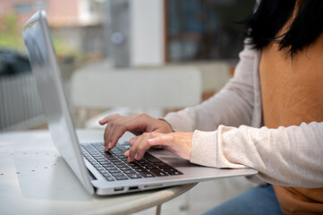 A cropped image of a woman types on her laptop keyboard, and works remotely at an outdoor table.