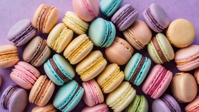 Multitude of colorful pastel French macaroons, tightly fitted together like delicious puzzle, standing upright at ends. Almond flavored. Banner has lilac background. Full-frame image. Top view.