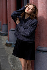 Young female model posing with closed eyes and leaning on column.