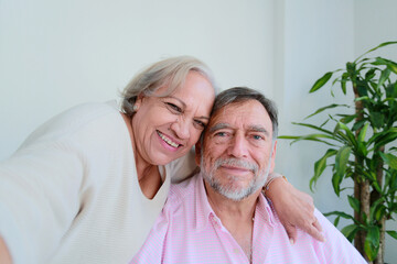 Older couple smiles while take a selfie with cell phone sitting at home