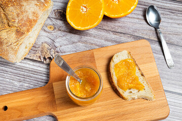 Delicious homemade orange jam in a glass jar on a wooden cutting board. Healthy breakfast with...