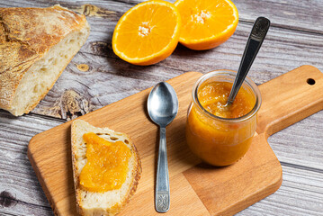 Delicious homemade orange jam in a glass jar on a wooden cutting board. Healthy breakfast with homemade orange jam