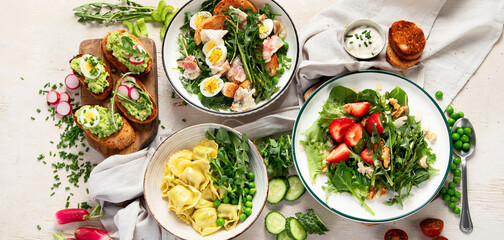 Spring fresh food with green leaf. Salads with strawberries, bacon and ravioli on light wooden background