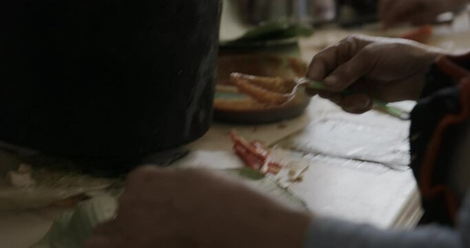 Woman putting food on large leaf and wrapping it up