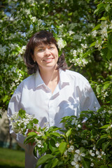 Girl walking and Relaxing near Blossoming apple Tree on Sunny Day. Portrait of Middle aged woman enjoying nature surrounded by white blossoms