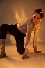 A stylish young queer person in vibrant attire crouching gracefully in front of a glowing light,...