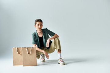 A young queer person sitting on the floor surrounded by colorful shopping bags in a studio on a...