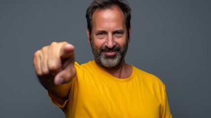 Naklejka premium A man, dressed in a yellow T-shirt, smiles and gestures at the camera with an uplifted hand