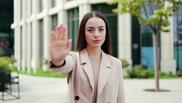 Skeptical woman extending hand to camera in negative gesture and saying no with stern emotions. Strict female showing refusal with disgusting expression while shaking head in denying outdoors.