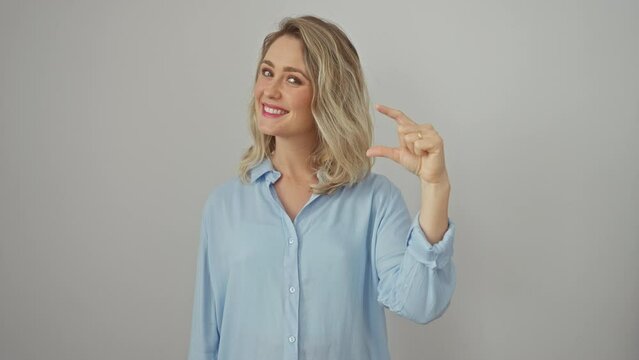 Confident blonde woman standing against white background, gesturing small size sign with fingers, measuring something with joy while wearing shirt.