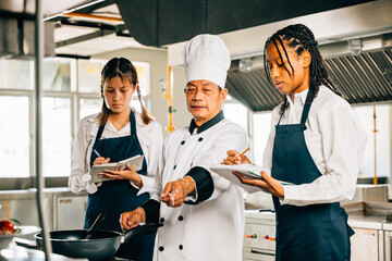 Senior Asian chef educates diverse students in a restaurant kitchen. Stressing teamwork learning...