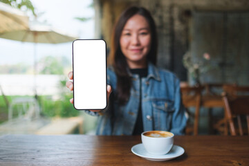 Mockup image of a woman showing a mobile phone with blank white screen in cafe