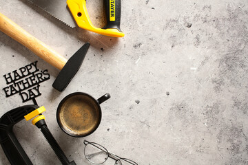 Father’s Day DIY Tools and Coffee - A thematic image perfect for Father’s Day promotions or articles. The scene includes a hammer, handsaw, eyeglasses, and a cup of coffee, arranged on a textured grey