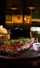 close up of pork ribs in barbecue sauce with parsley with a basket of rustic potatoes and bbq sauce with beer
