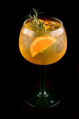 glass of tropical gin cocktail with orange and rosemary isolated on black background at angle