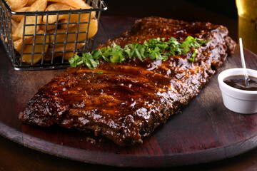 close up of pork ribs in barbecue sauce with parsley with basket of rustic potatoes and bbq sauce...