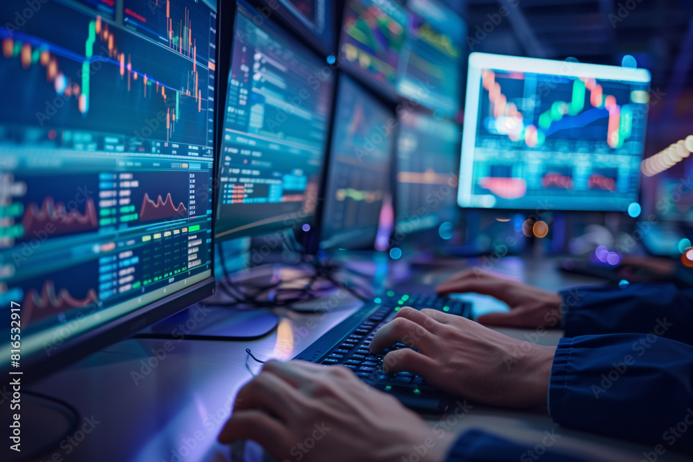 Wall mural A man is sitting in front of a computer monitor with multiple screens displaying financial data. He is typing on a keyboard, possibly working on a financial report or analyzing market trends