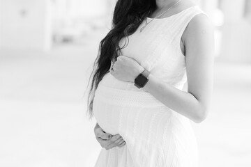 A black and white photo of a pregnant woman in a white dress cradling her stomach. 