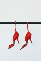 A pair of beautiful shape red high ankle strap heels hanging on the railisolate on white background