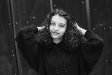 White brunette teenage girl with curly hair poses on the street in the city.