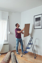 Man hanging pictures on the wall and cleaning, remodeling apartment.