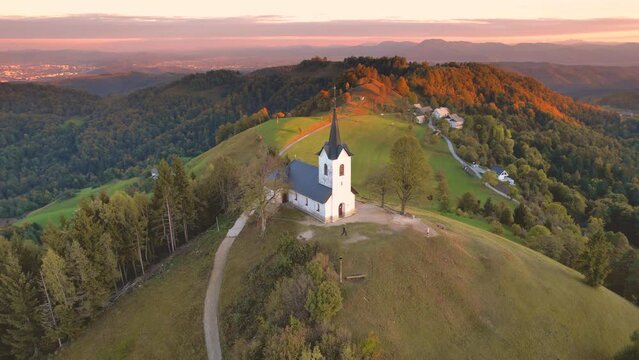 Aerial view of a colourful autumn sunset at Church of Saint Jacob (Sveti Jakob) in Medvode. Snowcapped mountains with the Karawanks, the Julian Alps and the Triglav, Medvode, Ljubljana, Slovenia