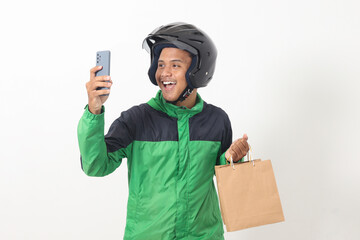 Portrait of Asian online courier driver wearing green jacket and helmet giving craft paper shopping...