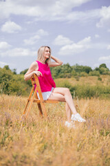 beautiful blonde woman posing on hair in field on hill.summer sunny day, girl in short pants and...