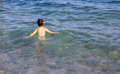 cute kid with hat on beach against sea or is having fun in summer vacation.boy with snorkel, diving set on eyes. child sprinkle with water, swimming, playing with boat ship toy, digging tools, bucket.