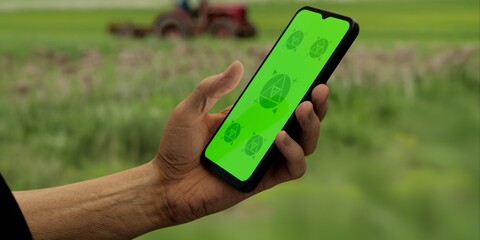 Hand holding a phone with a green screen against a farm backdrop